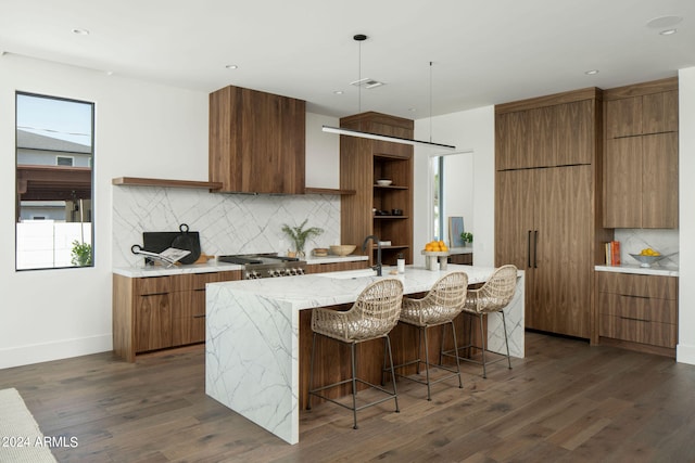 kitchen featuring a kitchen breakfast bar, a center island with sink, dark hardwood / wood-style flooring, backsplash, and pendant lighting