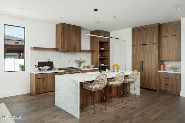 kitchen featuring hanging light fixtures, a center island with sink, dark hardwood / wood-style floors, backsplash, and a kitchen bar