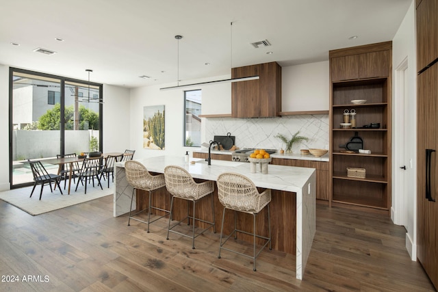 kitchen with a kitchen breakfast bar, dark wood-type flooring, a kitchen island with sink, pendant lighting, and tasteful backsplash