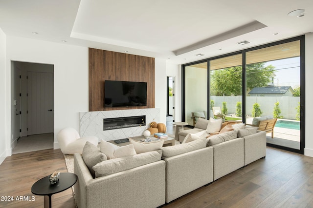 living room featuring floor to ceiling windows, a tray ceiling, a fireplace, and hardwood / wood-style flooring