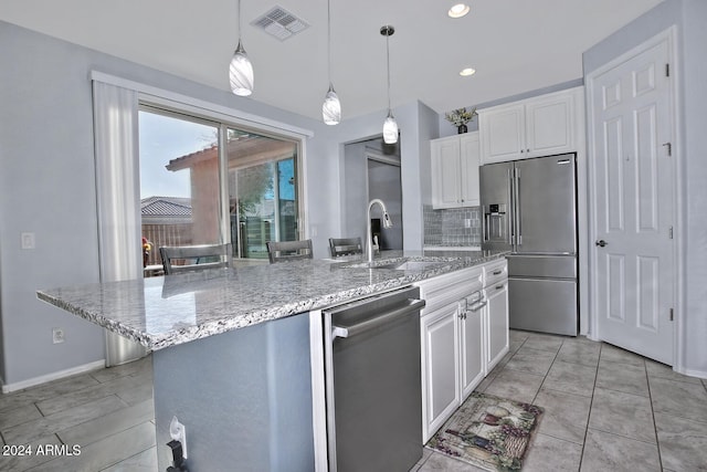 kitchen with white cabinetry, sink, stainless steel appliances, decorative light fixtures, and a center island with sink