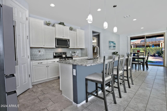 kitchen with white cabinets, light stone counters, stainless steel appliances, and a kitchen island with sink