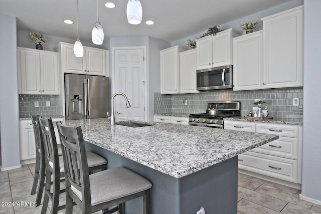 kitchen with sink, an island with sink, decorative light fixtures, white cabinets, and appliances with stainless steel finishes