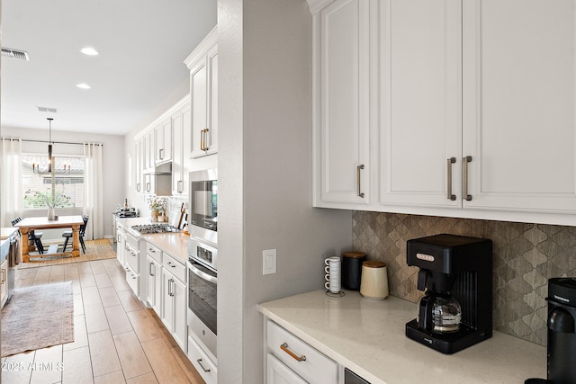 kitchen with white cabinets, a notable chandelier, stainless steel appliances, decorative backsplash, and visible vents