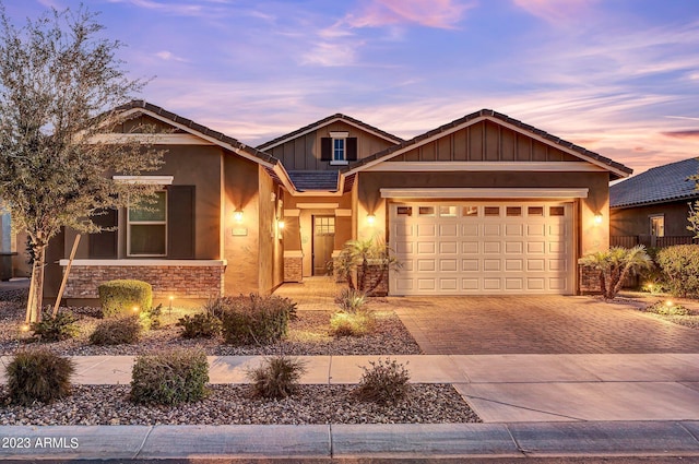 view of front facade featuring an attached garage, a tile roof, stone siding, stucco siding, and driveway