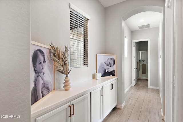 hall featuring visible vents, arched walkways, baseboards, and light wood-type flooring