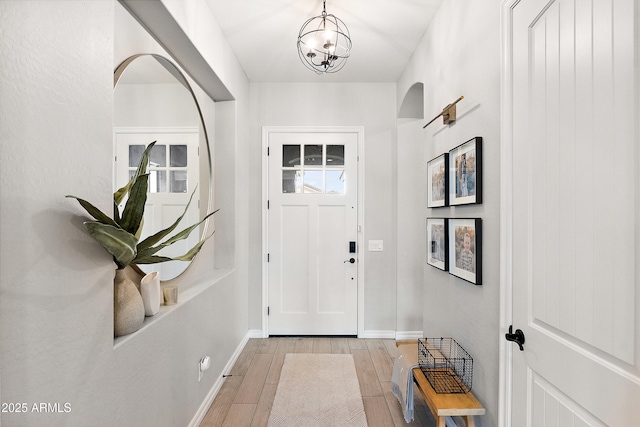 foyer entrance with baseboards, light wood-style flooring, and an inviting chandelier