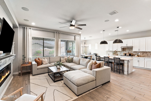 living room with visible vents, a glass covered fireplace, ceiling fan, light wood-type flooring, and recessed lighting