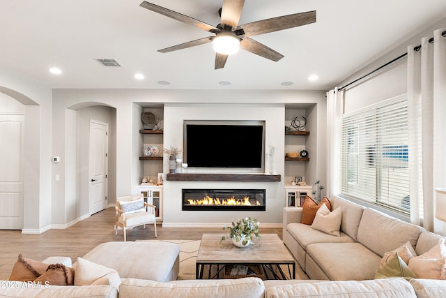 living room with arched walkways, a ceiling fan, built in features, and baseboards