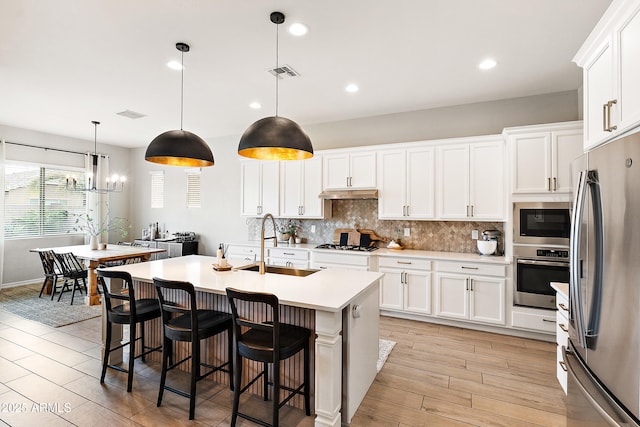 kitchen featuring visible vents, under cabinet range hood, a sink, appliances with stainless steel finishes, and backsplash