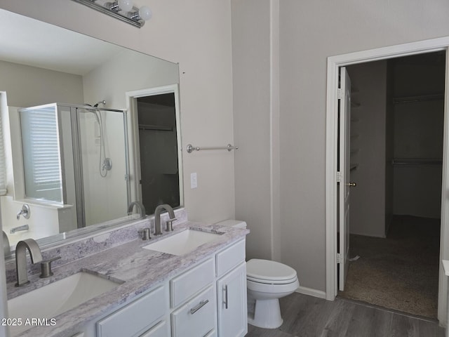 bathroom with wood finished floors, a sink, a walk in closet, and a stall shower
