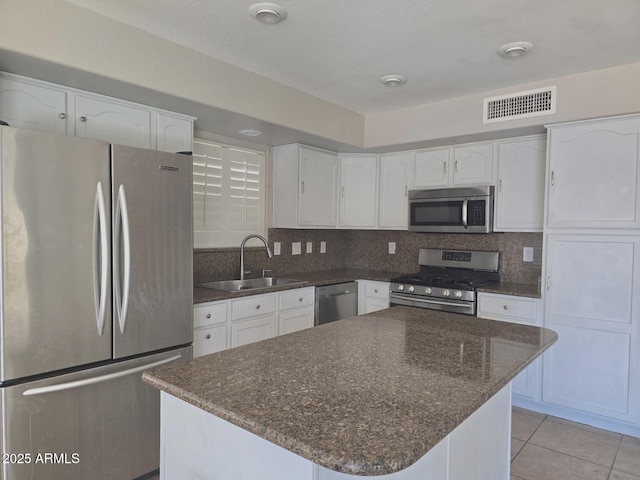 kitchen featuring visible vents, appliances with stainless steel finishes, a sink, white cabinets, and dark stone counters