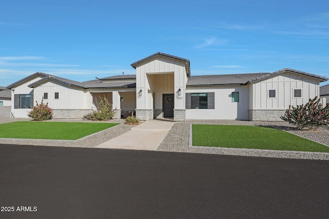 modern farmhouse style home featuring stone siding, a front lawn, and board and batten siding