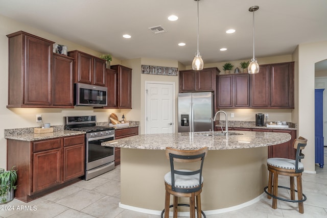 kitchen with a center island with sink, appliances with stainless steel finishes, light stone countertops, a kitchen bar, and sink