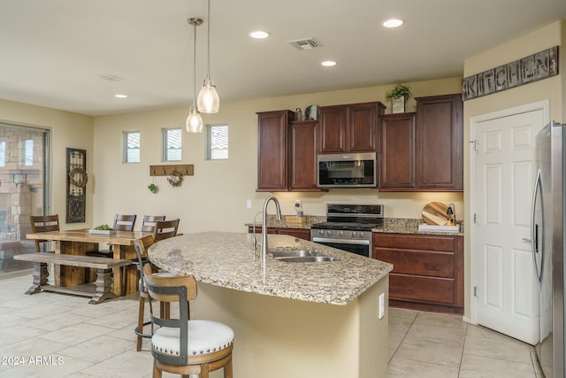 kitchen with hanging light fixtures, a center island with sink, light stone counters, appliances with stainless steel finishes, and sink