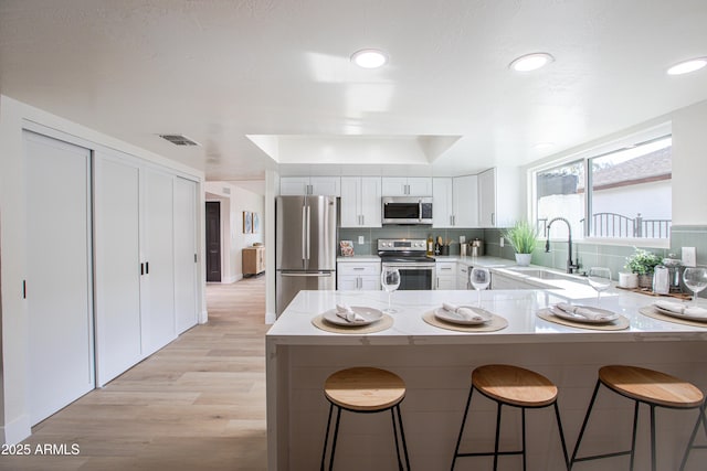 kitchen featuring appliances with stainless steel finishes, white cabinetry, sink, a kitchen breakfast bar, and kitchen peninsula