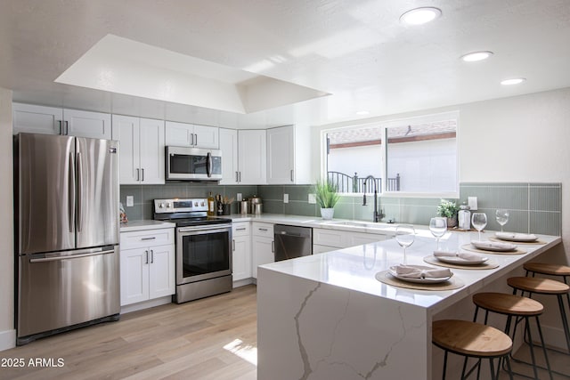 kitchen with sink, appliances with stainless steel finishes, light stone counters, white cabinets, and a kitchen bar