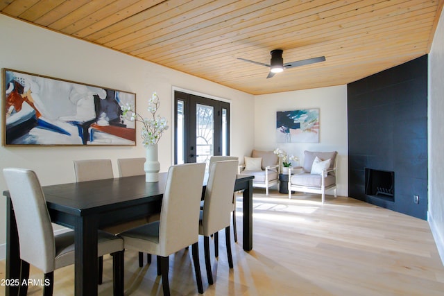 dining room with a fireplace, ceiling fan, light hardwood / wood-style floors, wooden ceiling, and french doors