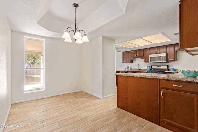 kitchen featuring sink, gas range oven, a raised ceiling, light hardwood / wood-style floors, and pendant lighting