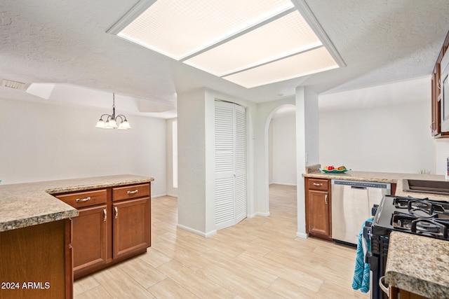 kitchen with light wood-type flooring, a textured ceiling, hanging light fixtures, stainless steel appliances, and a notable chandelier