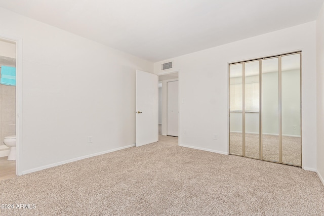 unfurnished bedroom featuring connected bathroom, light carpet, and a closet