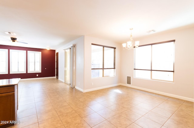 spare room with a healthy amount of sunlight, light tile patterned flooring, and ceiling fan with notable chandelier