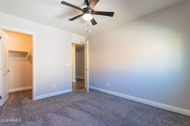 unfurnished bedroom with a closet, a spacious closet, dark carpet, and ceiling fan