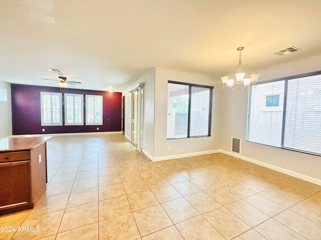 empty room with light tile patterned floors, a wealth of natural light, and ceiling fan with notable chandelier