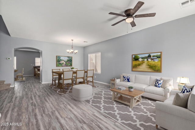 living area featuring arched walkways, visible vents, wood finished floors, baseboards, and ceiling fan with notable chandelier