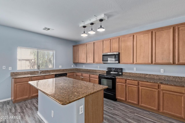 kitchen featuring appliances with stainless steel finishes, dark wood-type flooring, decorative light fixtures, a center island, and a sink