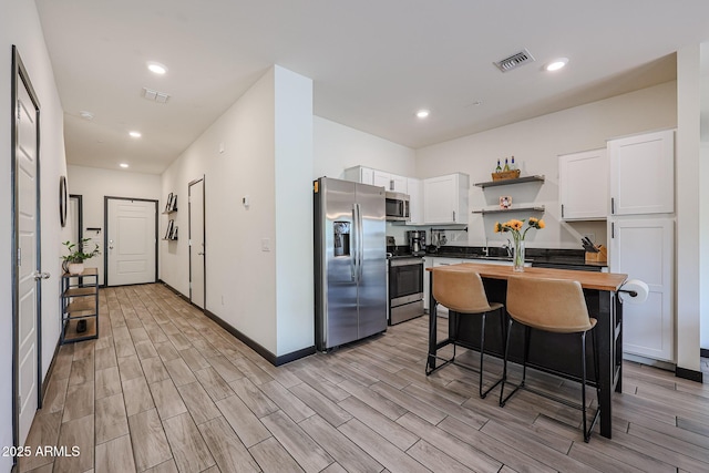 kitchen featuring butcher block counters, open shelves, stainless steel appliances, visible vents, and white cabinets