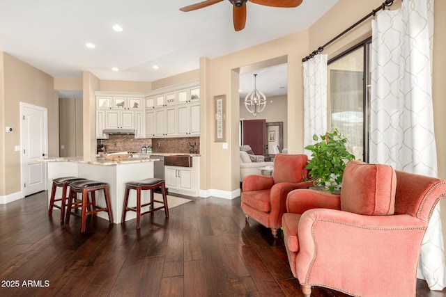 living area with baseboards, dark wood finished floors, and ceiling fan with notable chandelier