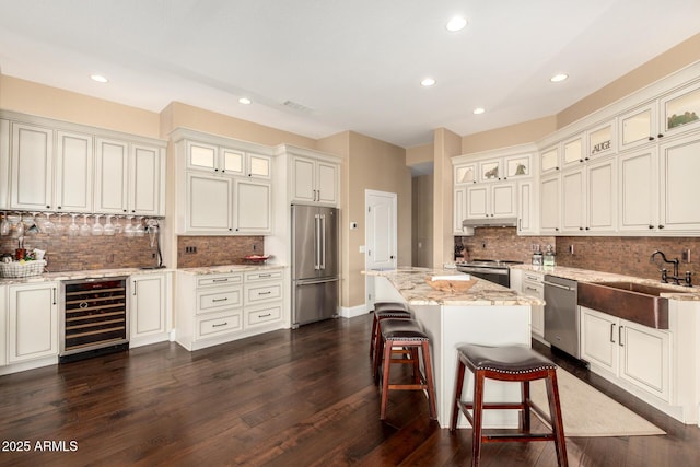 kitchen featuring decorative backsplash, appliances with stainless steel finishes, a sink, light stone counters, and beverage cooler