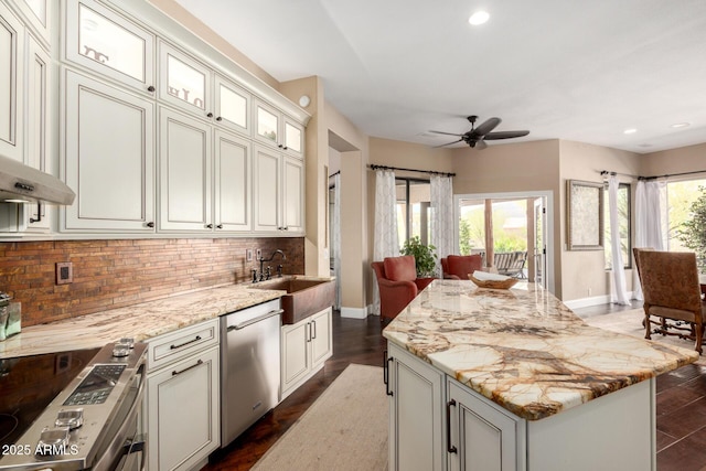 kitchen featuring ceiling fan, appliances with stainless steel finishes, a sink, a center island, and decorative backsplash