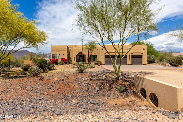 pueblo-style home featuring concrete driveway, an attached garage, and stucco siding