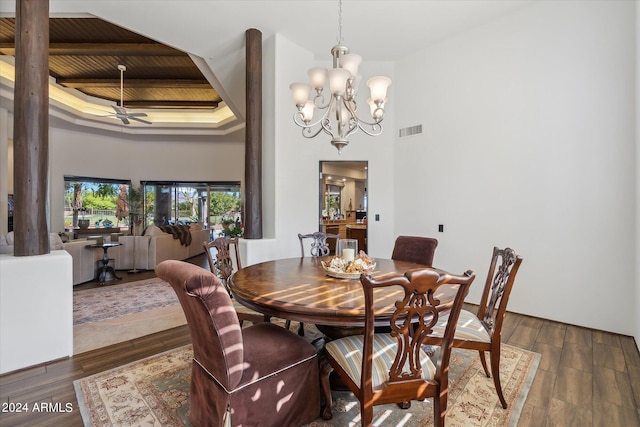 dining room with ceiling fan with notable chandelier, a tray ceiling, wood ceiling, dark wood-type flooring, and a towering ceiling