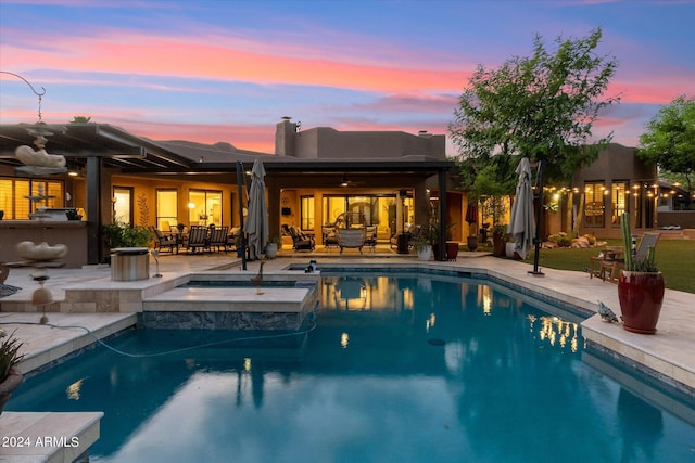 pool at dusk featuring a patio and an in ground hot tub