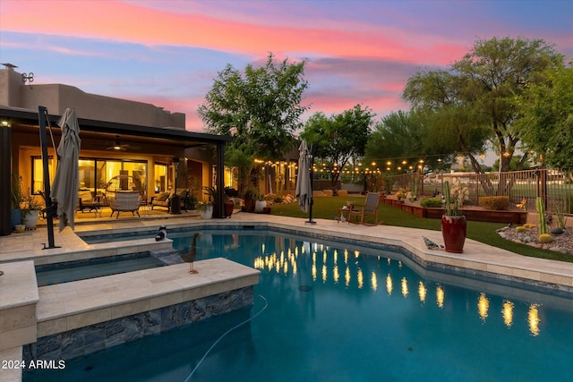 pool at dusk featuring an in ground hot tub and a patio