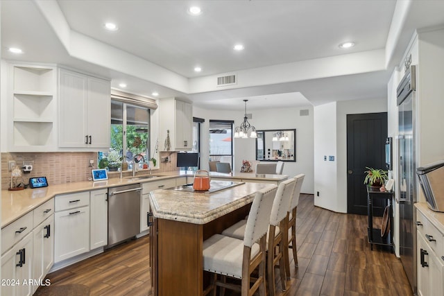 kitchen with stainless steel dishwasher, dark wood-type flooring, decorative backsplash, white cabinetry, and a chandelier