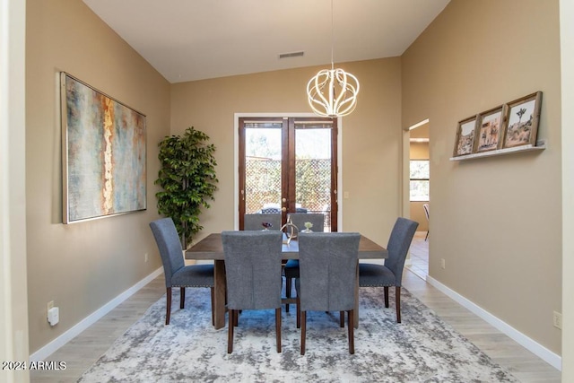 dining area with wood-type flooring, an inviting chandelier, and lofted ceiling