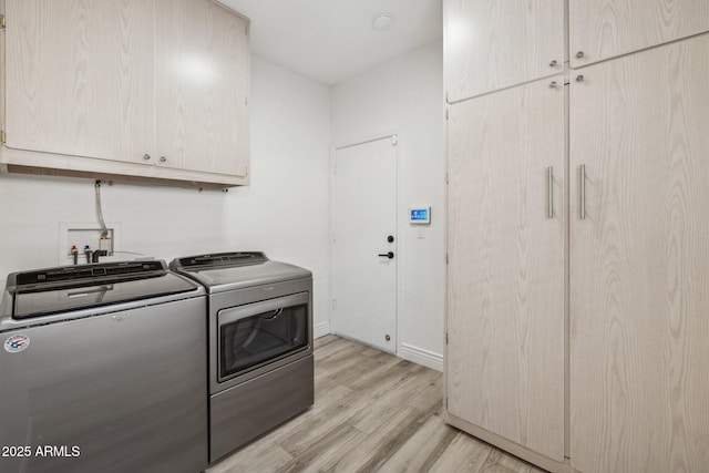 washroom with baseboards, cabinet space, light wood finished floors, and washing machine and clothes dryer