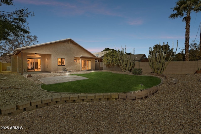 rear view of property featuring a patio area, a fenced backyard, a yard, and stucco siding