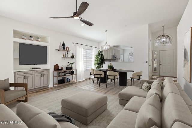 living room with lofted ceiling, light wood finished floors, arched walkways, and ceiling fan with notable chandelier