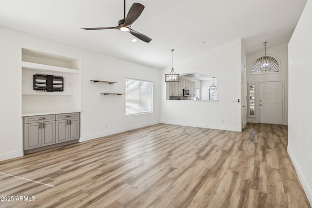 unfurnished living room featuring ceiling fan with notable chandelier, baseboards, and light wood-style floors