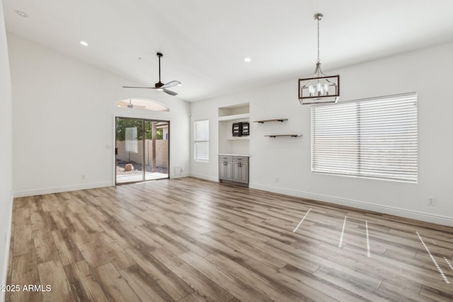 unfurnished living room with lofted ceiling, light wood-style flooring, recessed lighting, ceiling fan with notable chandelier, and baseboards