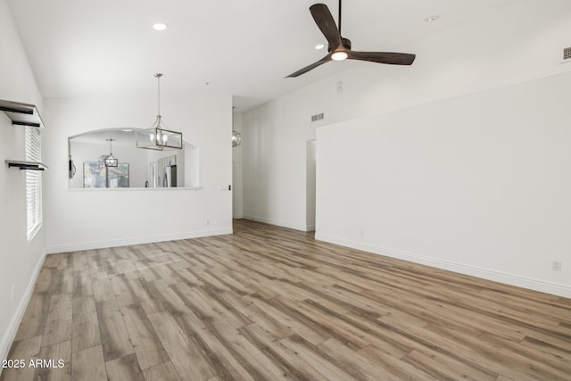 unfurnished living room with lofted ceiling, light wood-style flooring, baseboards, and ceiling fan with notable chandelier