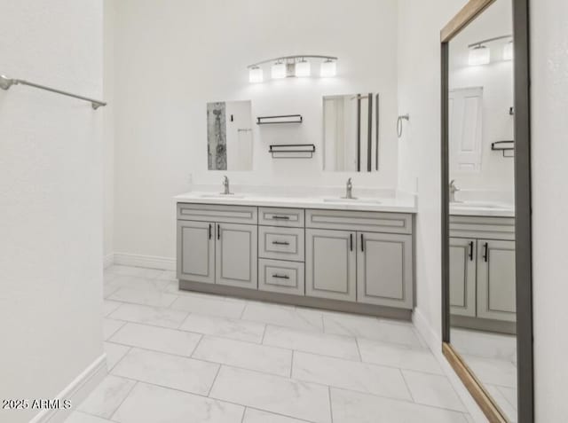 full bathroom featuring marble finish floor, a sink, baseboards, and double vanity