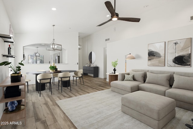 living area featuring high vaulted ceiling, light wood-style flooring, recessed lighting, ceiling fan with notable chandelier, and visible vents