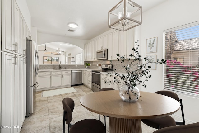 kitchen with a sink, white cabinetry, light countertops, appliances with stainless steel finishes, and pendant lighting