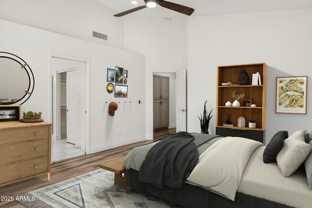 bedroom with visible vents, a towering ceiling, light wood-style floors, ceiling fan, and baseboards